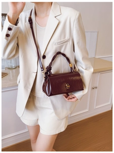 Detail of dark brown leather handbag featuring a twist handle and gold metal lock
