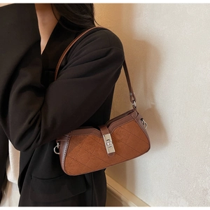 Detail of a brown quilted baguette bag with suede leather textures and metal buckle