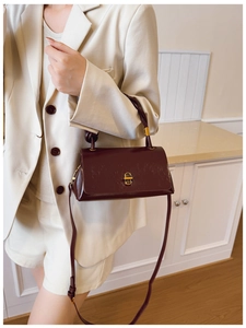 Detail of burgundy leather shoulder bag featuring a gold twist-lock and slim strap
