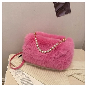 Detail of pink faux fur handbag with pearl chain and golden hardware on soft fabric