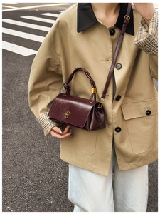 Detail of burgundy leather handbag with golden lock and twisted handle on trench coat