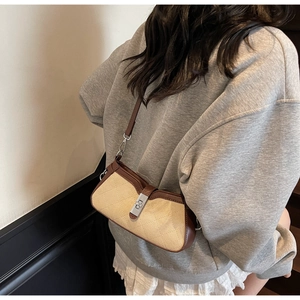 Detail view of a retro baguette bag with beige canvas and brown leather trim worn by model