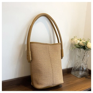 Détail du sac seau en paille tressée montrant la texture fine et les anses en cuir