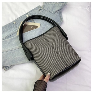 Détail du sac seau tissé avec poignée en cuir noir sur fond de tissu blanc texturé