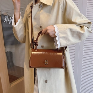 Detailed shot of brown patent leather bag featuring a gold geometric clasp and knotted handle