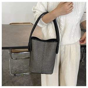 Détail du sac seau tressé présentant une texture noir et blanc et une anse en cuir