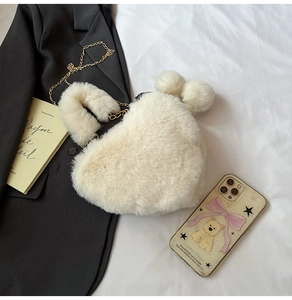 Detail einer cremefarbenen herzförmigen Kunstpelztasche mit goldener Kette und Pompons