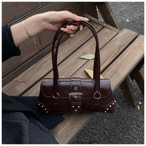 Detail of dark brown faux crocodile baguette bag with silver buckles on a wooden bench
