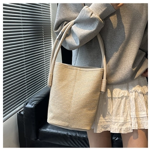 Détail du sac seau en paille tressée beige avec bandoulière en cuir porté par un mannequin