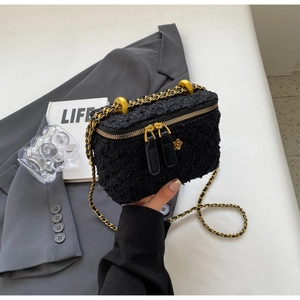 Close-up of black tweed bucket bag featuring gold hardware and a floral zipper charm