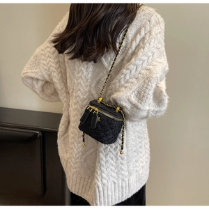 Close-up of black tweed mini chain box bag with gold zipper and flower charm on white sweater