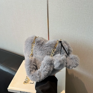 Graue herzförmige Plüschtasche mit goldener Kette und Kunstpelz-Textur auf dem Sofa