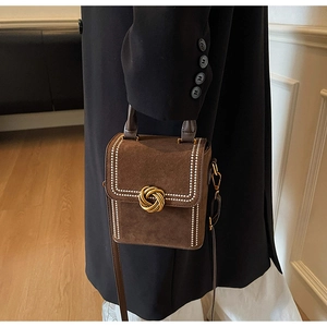 Detail of brown suede crossbody bag with gold stud trim and knot buckle on black coat
