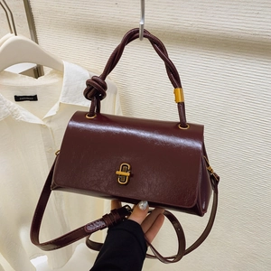 Deep wine red faux leather handbag with twisted handle and gold clasp on off-white background