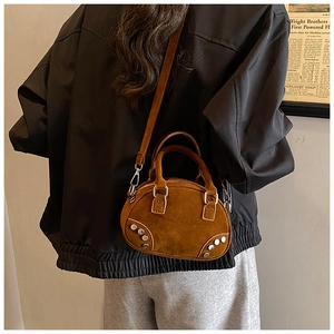 Close-up of brown suede bowling bag with silver rivet details and detachable shoulder strap