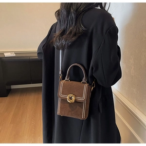 Detail of a dark brown suede crossbody bag featuring a golden spiral twist lock clasp