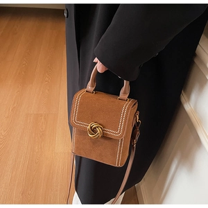 Detailed view of brown suede square handbag with gold twist lock and white contrast trim