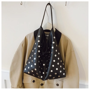 Detail of black tote bag with silver metal studs hanging against a trench coat background