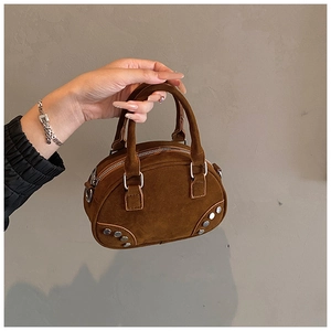 Close-up of brown suede bowling bag with silver studs and smooth metal zipper details