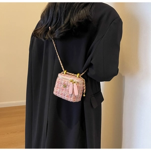 Close-up of pink tweed mini crossbody bag with golden camellia and chain strap on model