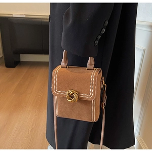 Detail showing brown suede texture, golden knot buckle, and pearl trim on the handbag