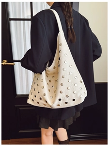 Detail of white leather shoulder bag with silver studs worn by a model in a black blazer
