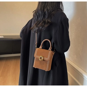Close-up of brown suede crossbody bag featuring gold twist lock and stitched flap detail