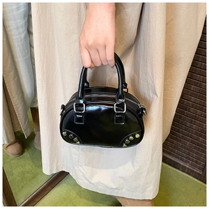 Detail of a black glossy leather bowling bag with gold studs and twin handles