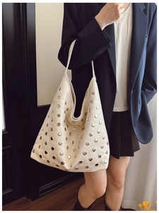 Detail of a large cream tote bag with silver metal studs and retro hobo silhouette