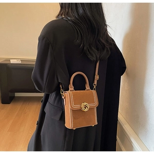 Detail of brown suede handbag with white bead trim and golden twist lock closure