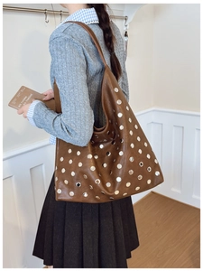 Brown hobo shoulder bag with silver studs and polished leather texture on model
