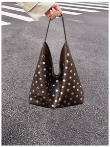 Close-up of a large dark brown hobo bag with silver rivets on a street background