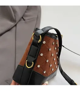 Detail of brown suede crossbody bag with diamond quilting and gold ring hardware