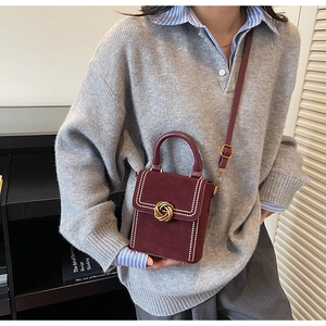 Detail view of burgundy suede handbag featuring decorative white studs and gold ring lock