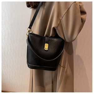 Sac seau noir texturé avec fermoir doré porté en bandoulière par un mannequin
