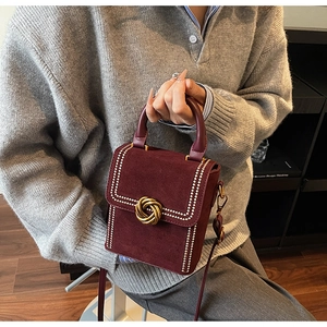 Close-up of burgundy suede crossbody bag with gold knot buckle and pearl trim details