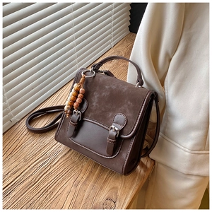 Dettaglio borsa a tracolla marrone vintage con ciondolo in legno e pelle liscia