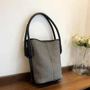 Sac seau tissé minimaliste bicolore avec lanières en cuir noir sur une table en bois massif