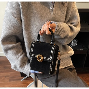 Detail of black velvet handbag featuring a gold rope-knot buckle and leather handle