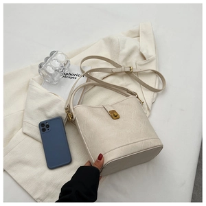 Détail du sac seau crème avec fermoir rotatif doré sur une veste de costume blanche