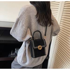 Detail of a black retro mini bag with white pearl trim and gold circular metal lock
