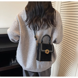 Close-up of black suede crossbody bag with pearl bead trim and gold woven metal buckle