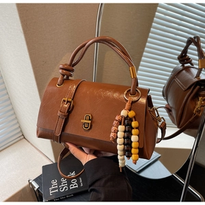 Détail du sac baguette en cuir marron vintage avec fermoir métallique et breloque perlée