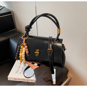 Gros plan détaillé d'un sac baguette noir brillant avec bandoulière nouée et boucle dorée