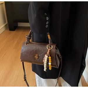 Détail du sac en cuir marron foncé avec fermoir doré vintage et breloque perlée