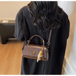 Detail view of brown matte leather baguette bag with beaded charm on the handle
