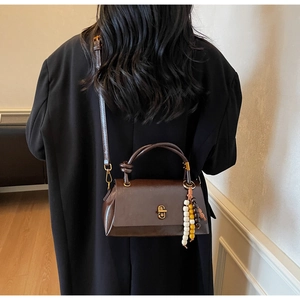 Détail du sac baguette rétro marron foncé avec boucle dorée et pendentif en perles