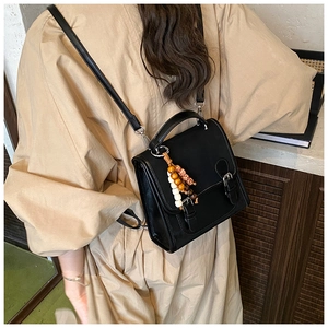 Dettaglio di zaino vintage in pelle nera con perline decorative su un trench coat beige
