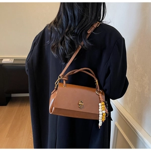 Brown leather handbag with beaded charm shown on model in minimalist interior
