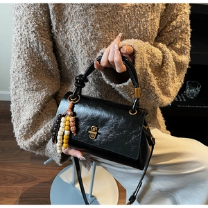 Détail du sac en similicuir noir avec poignée tressée et charm en perles de bois colorées